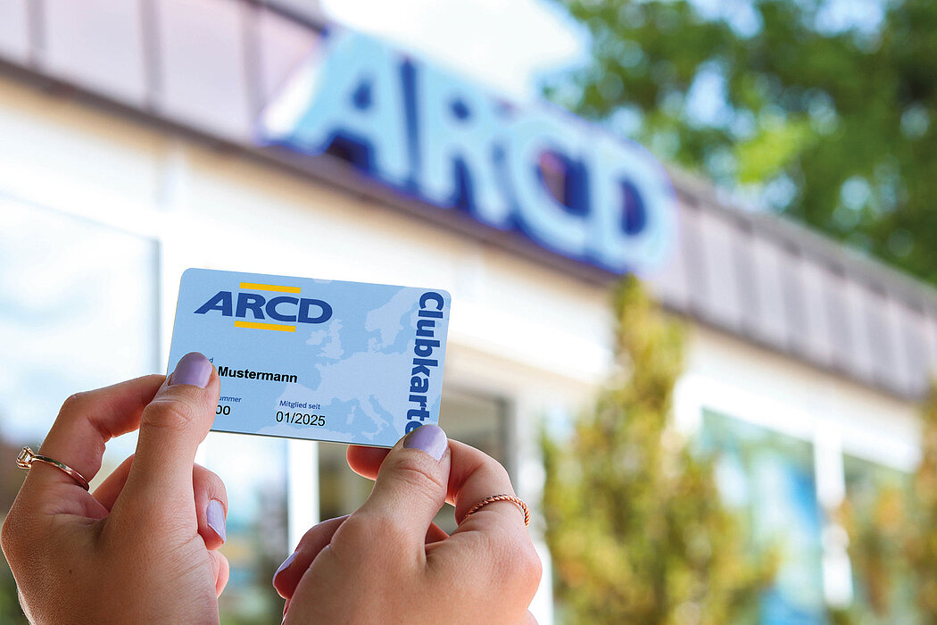 Eine Hand hält die ARCD-Clubkarte vor dem ARCD-Gebäude.