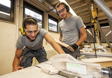 Zwei Personen arbeiten sicher und konzentriert an einer Tischkreissäge in einer gut ausgestatteten Holzwerkstatt – Teamarbeit und Präzision im Handwerk